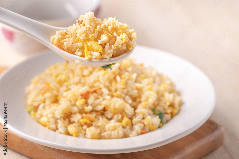 Eating Chinese fried rice in white plate on bright wooden table background.