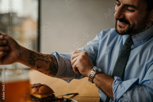 Attractive businessman rolling up his sleeves on his shirt, preparing for relaxation with a beer and burger.