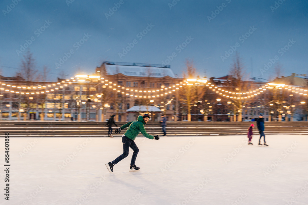 Obraz premium Horizontal shot of active man uses ice skates for going in for sport on ice ring, spends winter holidays actively, demonstrates professionalism and speed. Male ice skating outdoors