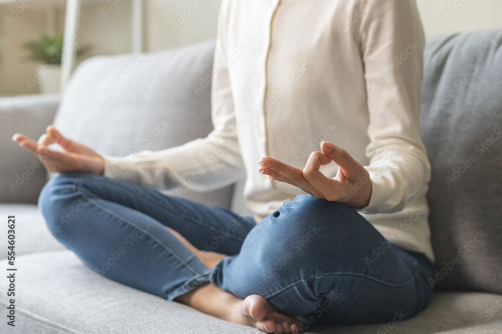 Beautiful asian young woman, girl hands in calm pose sitting practice meditating in lotus position on sofa at home, meditation, exercise for wellbeing, healthy care. Relaxation, happy leisure people.