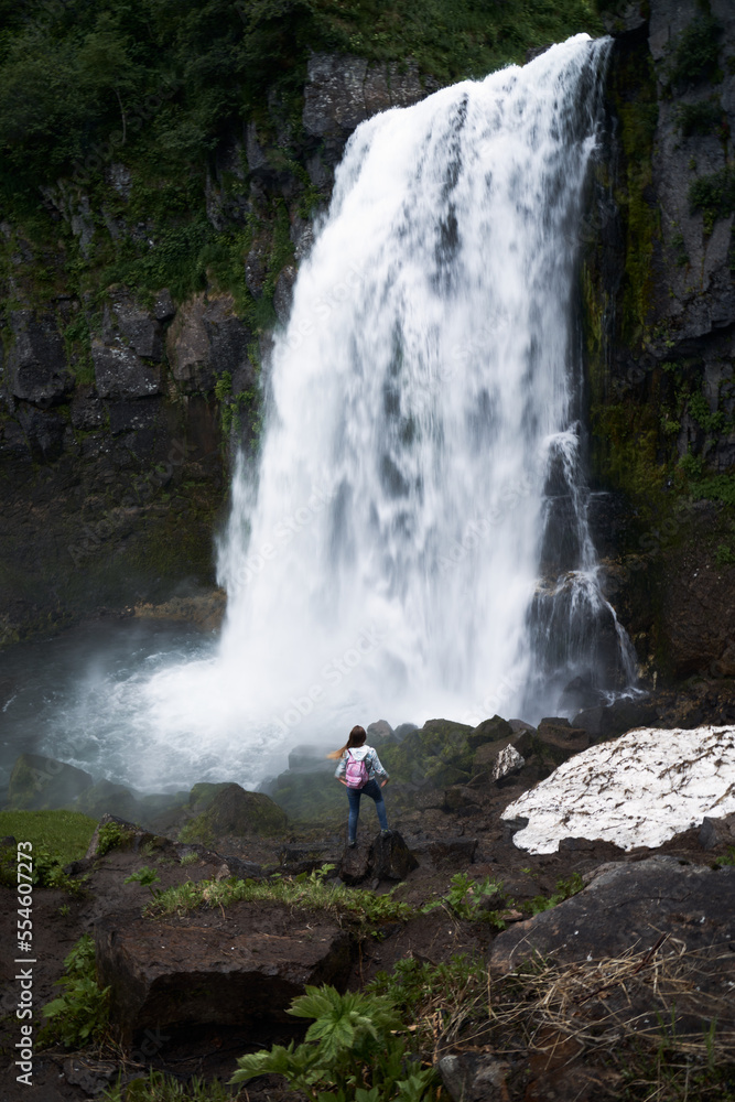 Female hiker standing if front of the waterfall. Traveling through Kamchatka peninsula
