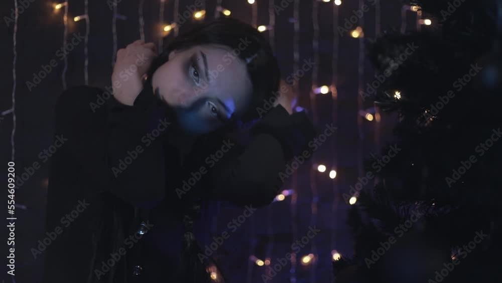 Creepy girl writhing near the black Christmas tree, looking at the camera. Horror movie. Creepy girl writhing near the black Christmas tree, looking at the camera. Horror movie.