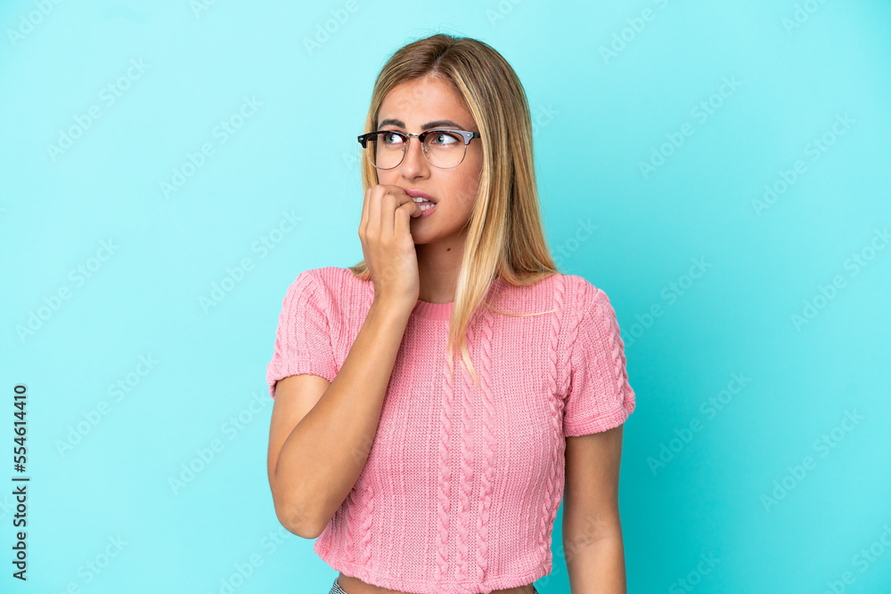 Blonde Uruguayan girl isolated on blue background is a little bit nervous Blonde Uruguayan girl isolated on blue background is a little bit nervous