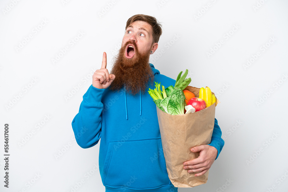 Redhead man with beard holding a grocery shopping bag isolated on white background thinking an idea pointing the finger up Redhead man with beard holding a grocery shopping bag isolated on white background thinking an idea pointing the finger up