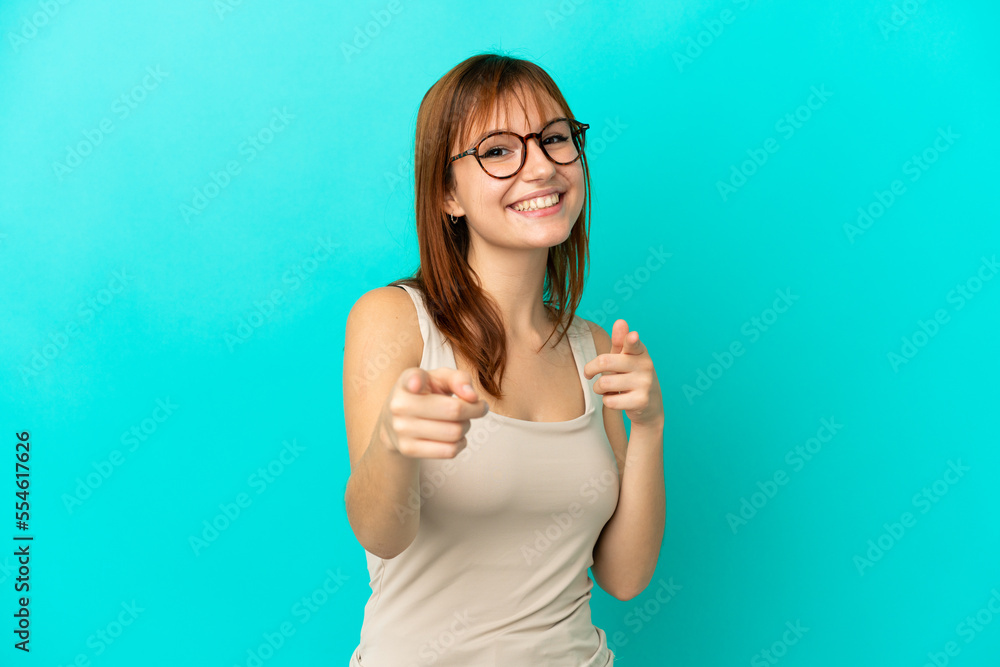 Fototapeta premium Redhead girl isolated on blue background surprised and pointing front