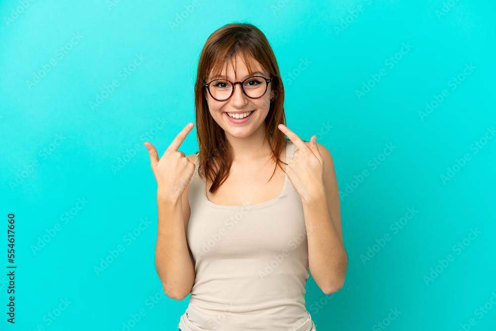 Redhead girl isolated on blue background giving a thumbs up gesture Redhead girl isolated on blue background giving a thumbs up gesture