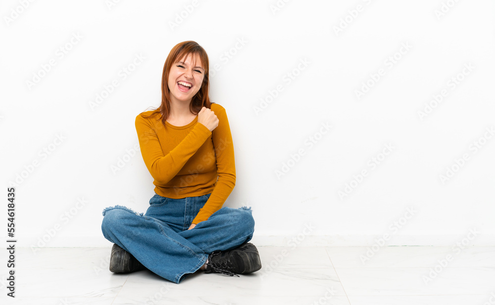 Redhead girl sitting on the floor isolated on white background celebrating a victory Redhead girl sitting on the floor isolated on white background celebrating a victory