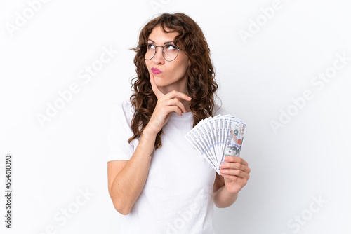 Young woman with curly hair taking a lot of money isolated background on white background having doubts while looking up
