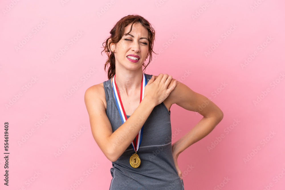 Young caucasian woman with medals isolated on pink background suffering from pain in shoulder for having made an effort Young caucasian woman with medals isolated on pink background suffering from pain in shoulder for having made an effort