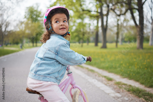 Fototapeta Naklejka Na Ścianę i Meble -  Kids, bike and learning to ride with a girl in the park on her bicycle while wearing a helmet for safety outdoor. Summer, cycling and children with a happy female child training to cycle in a garden
