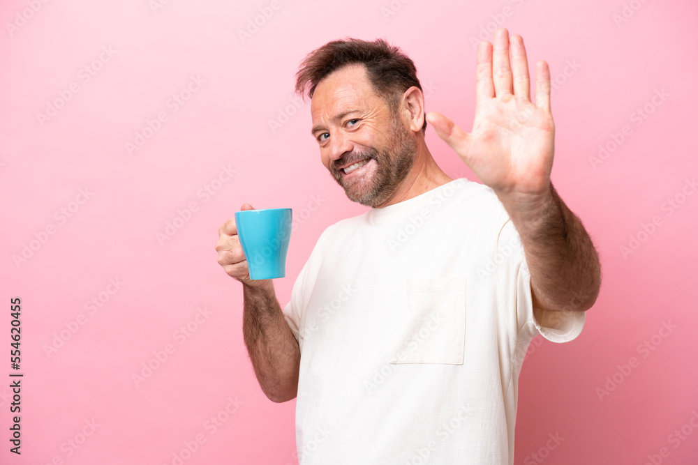 Middle age caucasian man holding cup of coffee isolated on pink background saluting with hand with happy expression Middle age caucasian man holding cup of coffee isolated on pink background saluting with hand with happy expression