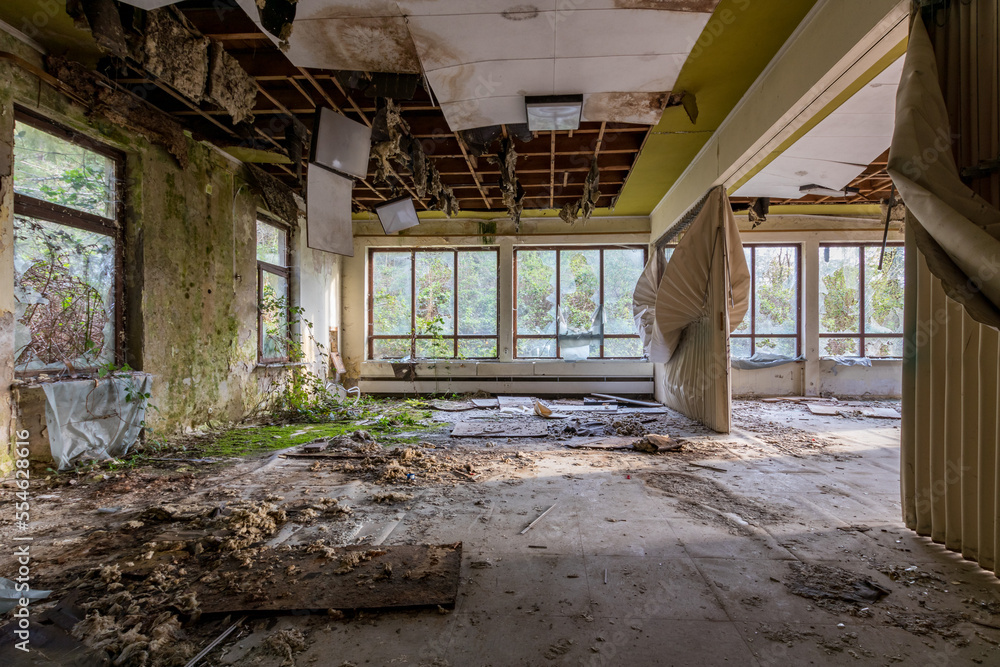An abandoned psychiatric ward, a large room with broken ceiling, moss growing on the floor.