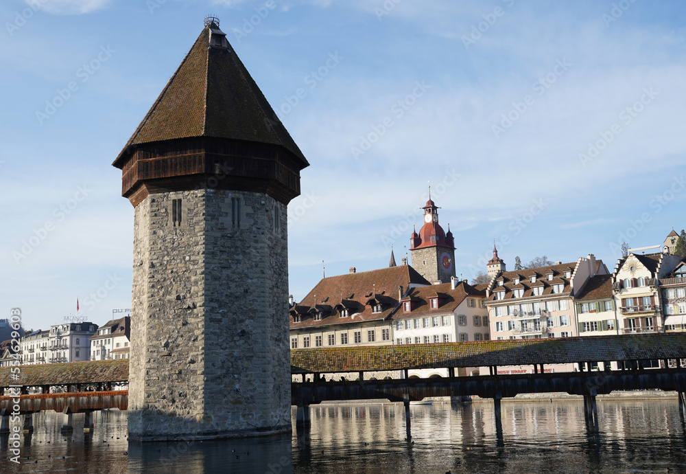 Water Tower and Chapel Bridge over river Reuss in Lucerne in Switzerland. Behind are historical buildings and a landmark of the city attracting tourists. 