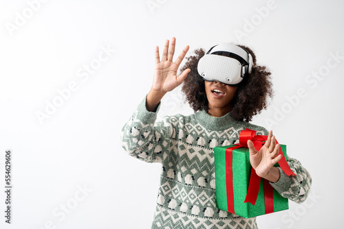 Portrait of young attractive african american woman curly hair with VR goggles holding gift box in studio on white background. © Jirus