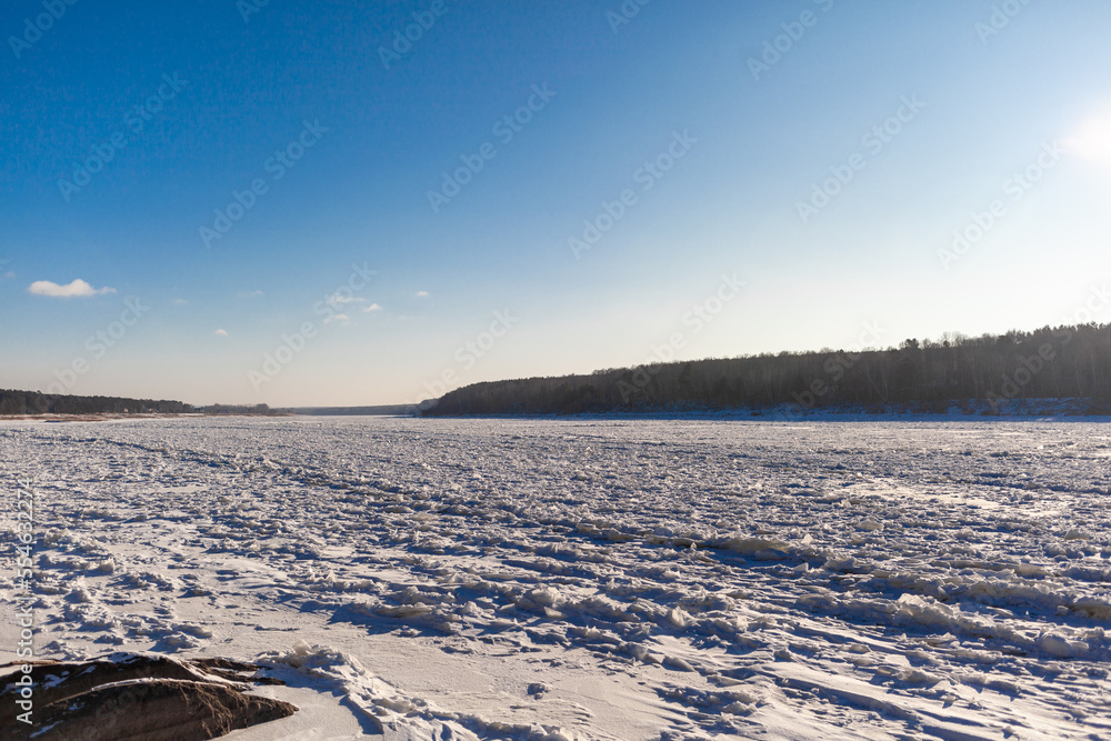 Obraz premium A frozen lake or river in winter. Near the forest and mountains in the snow. Beautiful winter landscapes. Winter trips in nature.