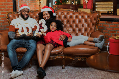 Happy African American family mother, father and adorable daughter on couch resting together. Little girl sleep on mother legs relax in living room with Christmas decorations at home.