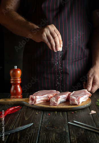 Professional chef sprinkles raw ribs with salt. The concept of cooking delicious food for the hotel or restaurant