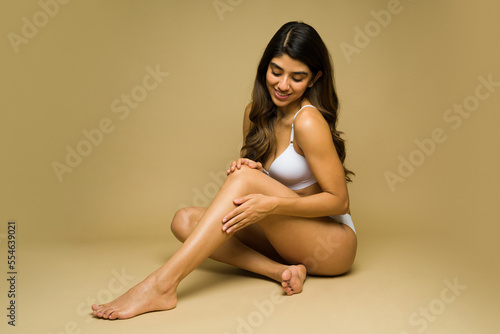 Fit young woman moisturizing her body and legs