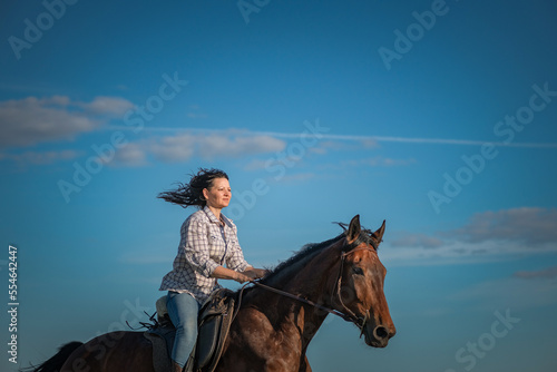 Молодая красивая тёмноволосая девушка скачет на лошади по летнему полю.