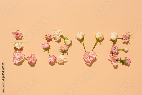 Flower composition. Love is a word of white roses on a beige pastel background. top view. The concept of congratulations, confessions of feelings. Valentine's Day greeting card. Flat vintage layout