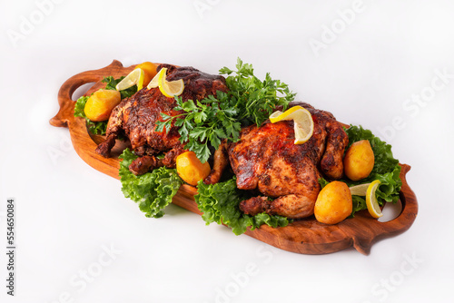 two fried chicken with potatoes, herbs and lemon on a wooden platter on a white background