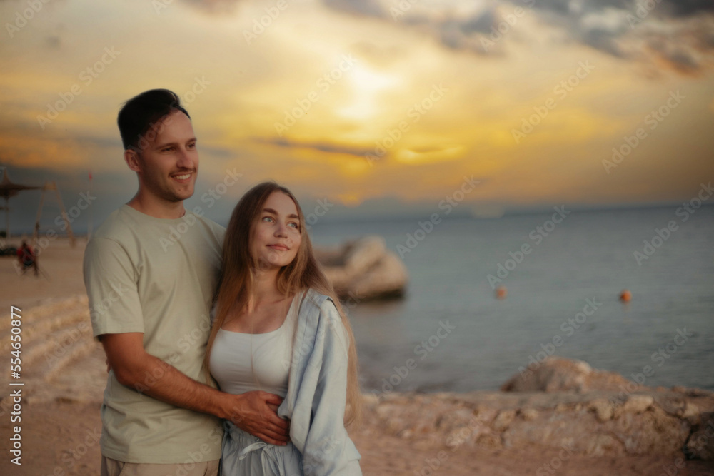 young couple in love at sunset by the sea walk along the seashore. Romantic trip to the resort.