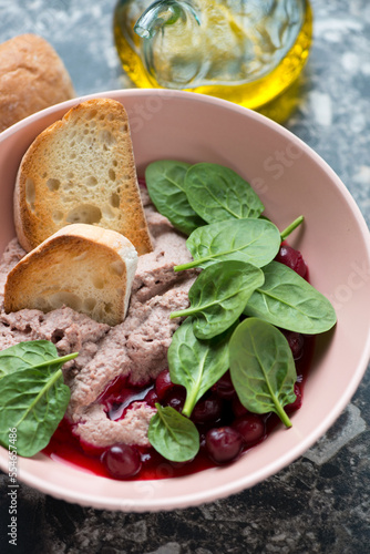Close-up of liver pate with cranberry sauce, fresh spinach and ciabatta served in a roseate bowl, vertical shot