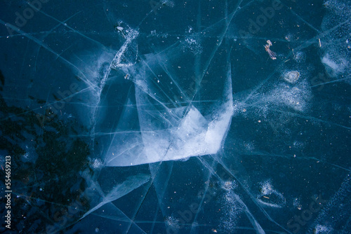 blue ice on the lake with a white impact mark and cracks radiating from it in the winter in the frost during the day
