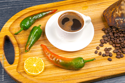 Freshly brewed hot black coffee in a white cup on a wooden board with coffee beans. hot pepper