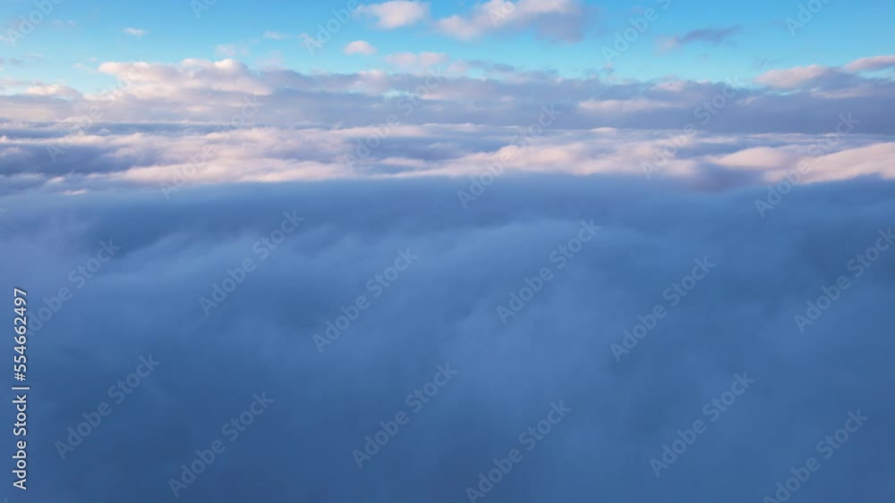 Flying among the ocean of clouds in the mountains. The fog is like big ocean waves crashing against high mountains covered with snow. Spruce trees grow in places. Sunset. Orange rays of the sun Flying among the ocean of clouds in the mountains. The fog is like big ocean waves crashing against high mountains covered with snow. Spruce trees grow in places. Sunset. Orange rays of the sun