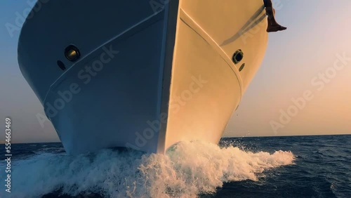 Sailboat prow breaking sea water front view, white foam and splashes close up. Yachting, ocean sailing, sunset sun light on vessel part, boat forepart closeup