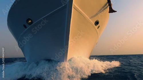 Sailboat prow breaking sea water front view, white foam and splashes close up. Yachting, ocean sailing, sunset sun light on vessel part, boat forepart closeup photo