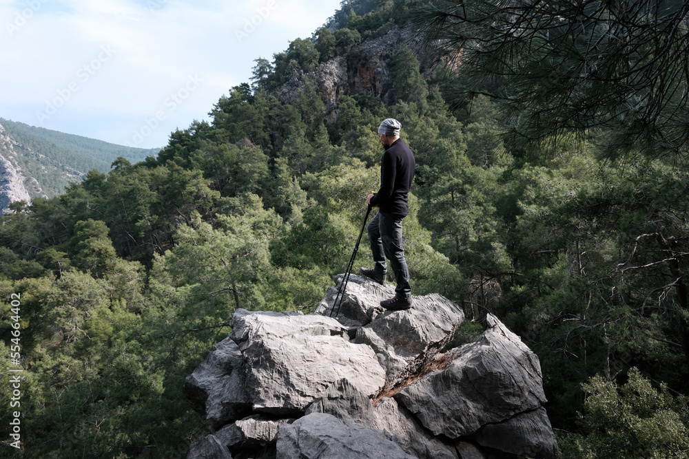 A hiker (Caucasian man) with trekking poles stand on the rock above the forest in the mountains on winter day. Goynuk gorge, Lycian way, Turkey. A hiker (Caucasian man) with trekking poles stand on the rock above the forest in the mountains on winter day. Goynuk gorge, Lycian way, Turkey.