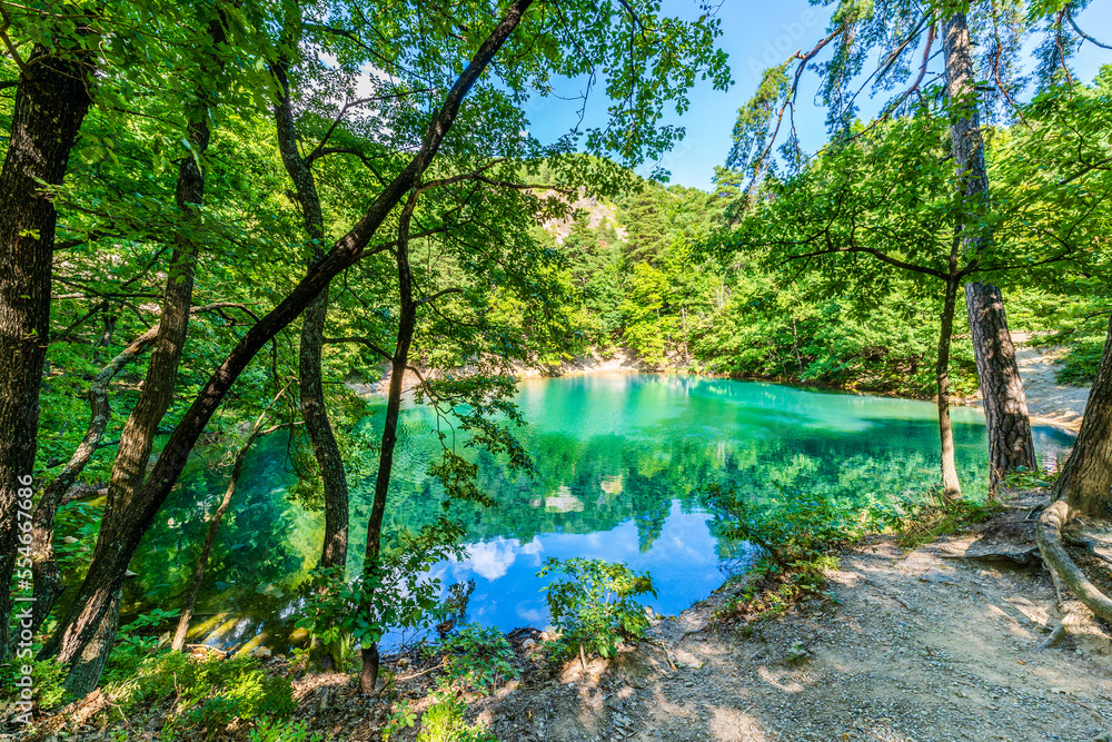 Blue Lake in Baia Sprie, Maramures, Romania; blue green lake surrounded by green trees in the forest Blue Lake in Baia Sprie, Maramures, Romania; blue green lake surrounded by green trees in the forest