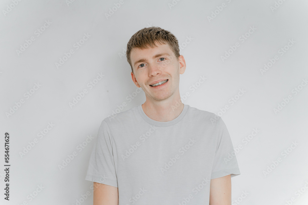 a man in a gray t-shirt on a white wall stands smiling with braces a man in a gray t-shirt on a white wall stands smiling with braces