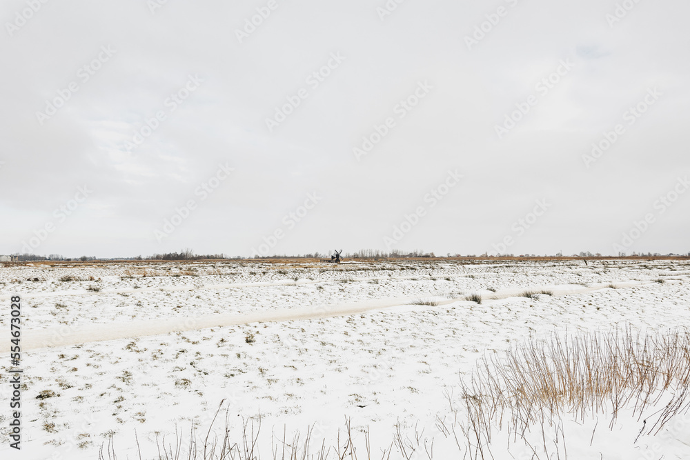 Dutch winter landscape with a small water mill on the horizon.