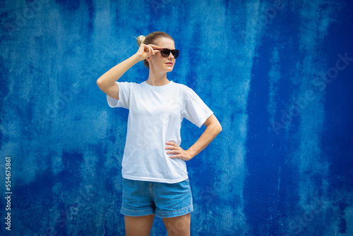 Female model wearing white blank t-shirt on the background of an blue wall. © romaset