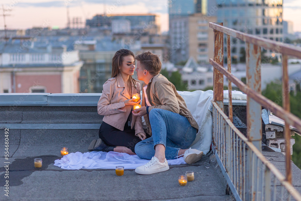 Beautiful young loving couple on a surprise date on a Saint Valentine's Day on a rooftop. Romantic picnic with candles. Newlyweds. Panoramic view, urban cityscape with skyscrapers on background