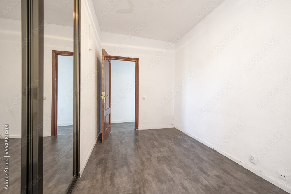 An empty room with a built-in wardrobe with sliding mirror doors with ocher anodized aluminum edges and gray wooden floors An empty room with a built-in wardrobe with sliding mirror doors with ocher anodized aluminum edges and gray wooden floors