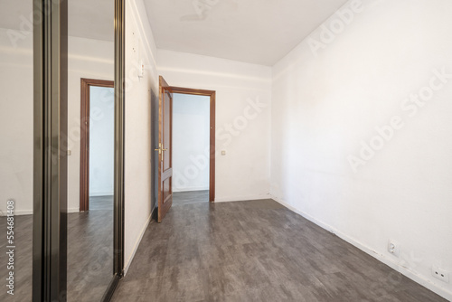 An empty room with a built-in wardrobe with sliding mirror doors with ocher anodized aluminum edges and gray wooden floors