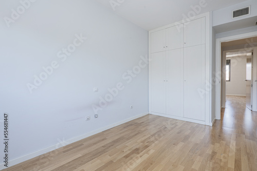 An empty room with a three-section built-in wardrobe with white doors and a mezzanine with a trunk  oak parquet floors and light white walls