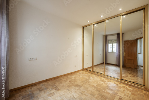 Empty room with a built-in wardrobe with sliding mirror doors and golden metal edges