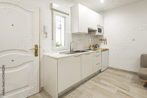 Small open kitchen in a living room of a studio with a small window and the white front door