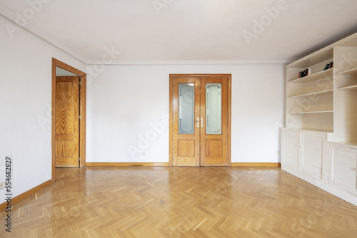 Empty room with wooden double doors with beveled glass and white bookshelf on one wall.