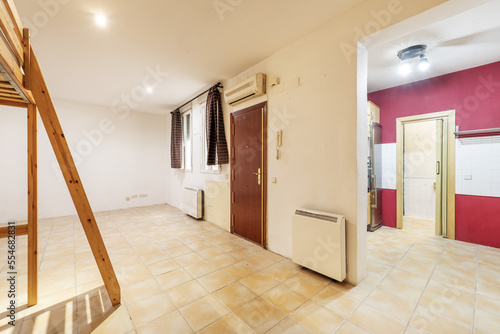 Room of a facio studio apartment with accumulator heat and access without doors to a kitchen with red walls and white tiles photo