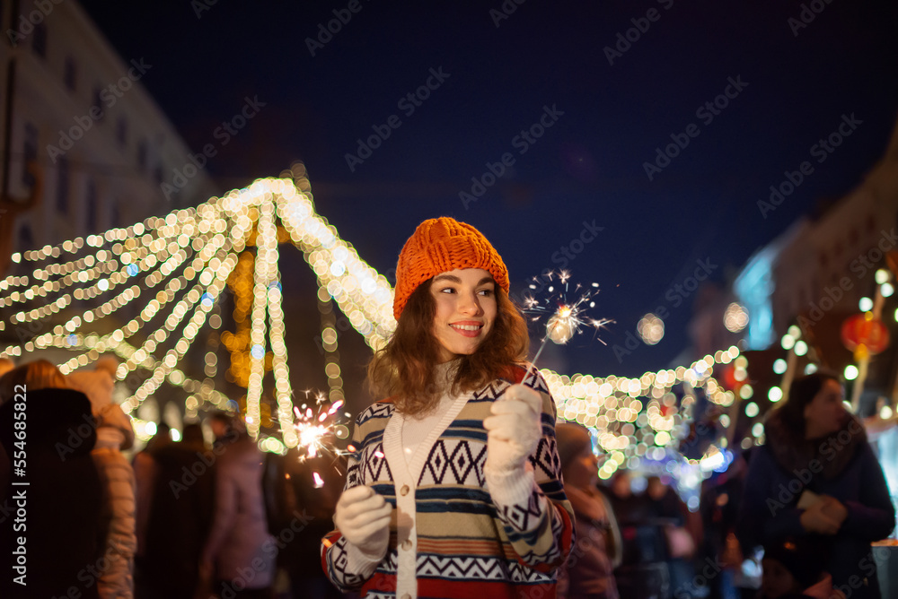 Happy smiling woman holding sparklers, posing at street festive Christmas fair in European city. Outdoor night portrait. Copy, empty space for text