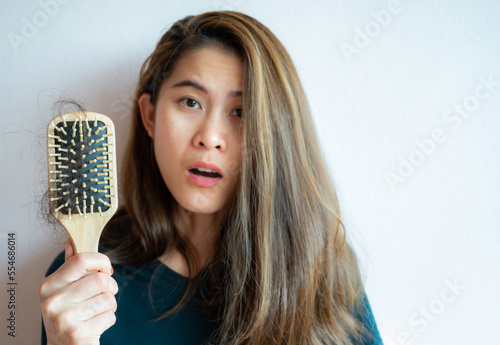 Asian worried woman holding comb with hair loss after brushing her hair.