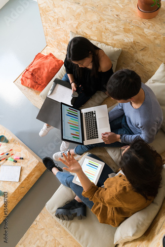 From above shot of Asian people sitting on couch with laptop and tablet watching graphics.