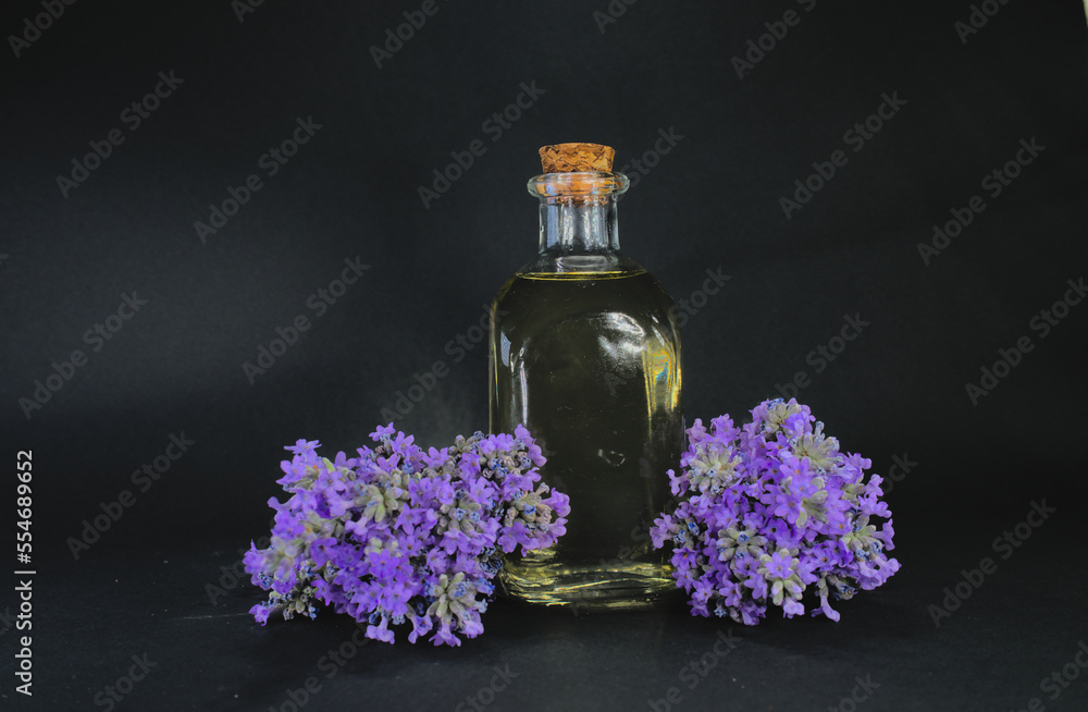 Lavender oil in glass bottle near fresh lavender flowers on black background Lavender oil in glass bottle near fresh lavender flowers on black background