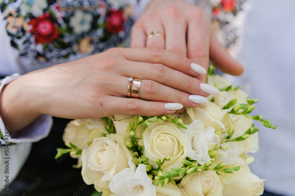 Golden wedding rings on the hands of the newlyweds. Man and woman in national Ukrainian clothes. Bridal bouquet with white flowers Golden wedding rings on the hands of the newlyweds. Man and woman in national Ukrainian clothes. Bridal bouquet with white flowers